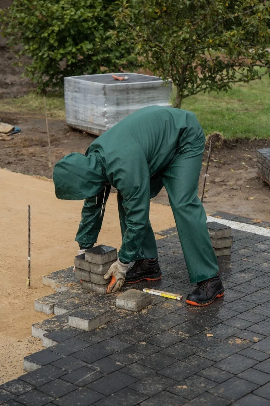 A crew member in green waterproofs laying paving on a wet day, seen from behind