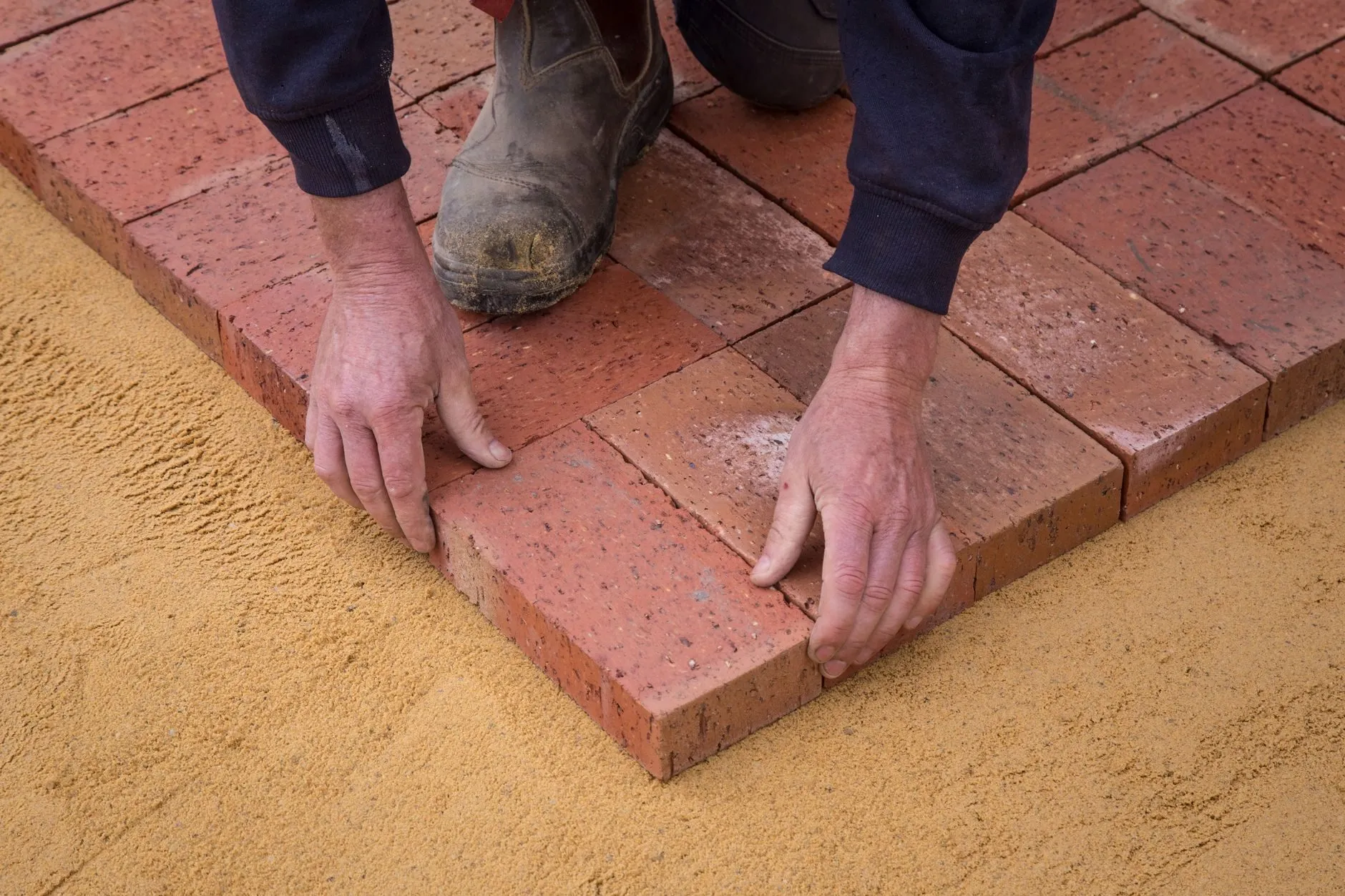 Hands setting clay pavers onto a sharp sand bed