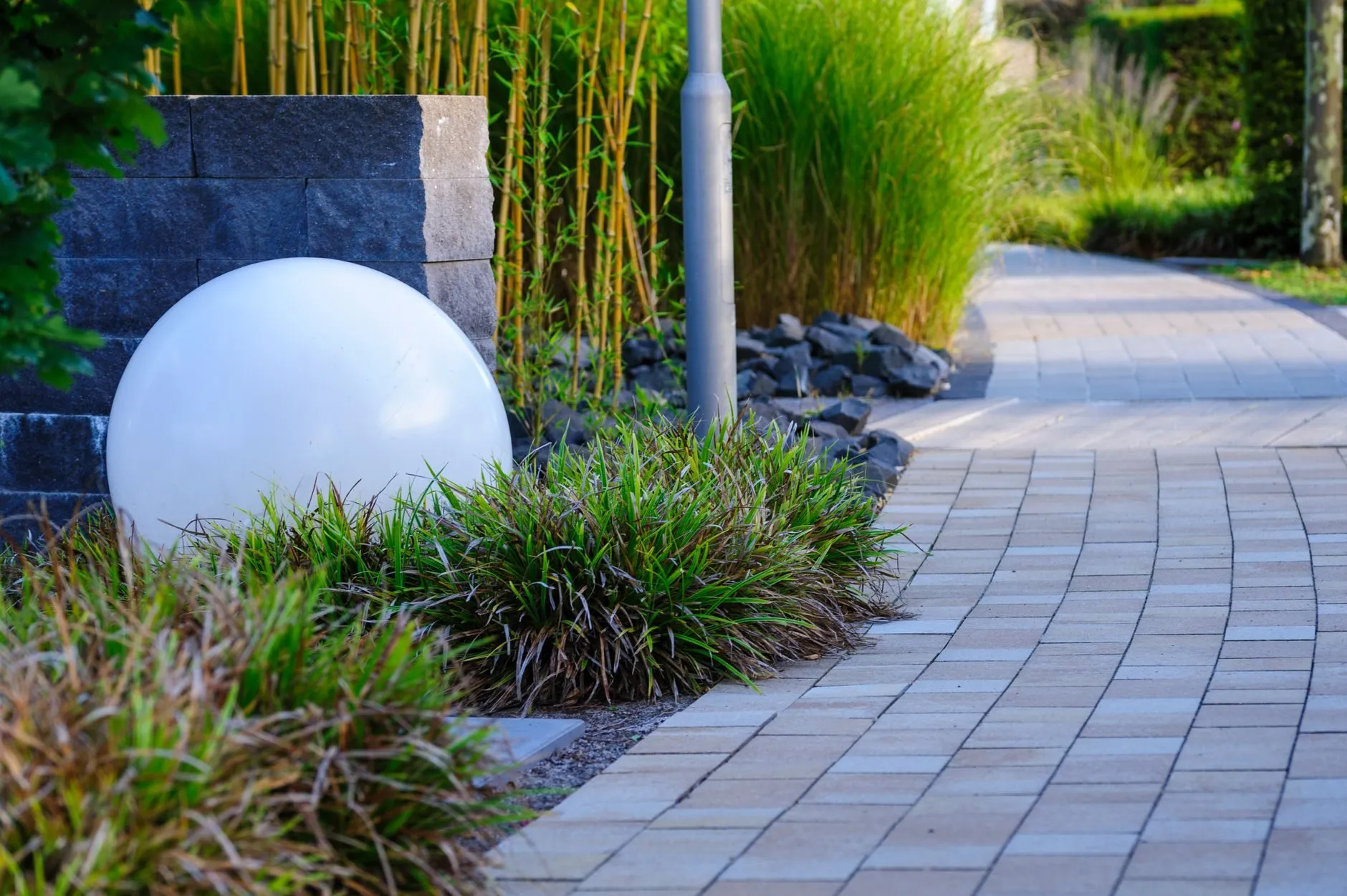 A curved block-paved path with a globe light and ornamental grasses