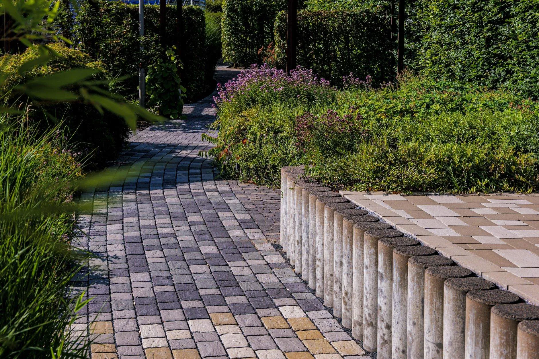 A finished block-paved path curving between low walls and planting
