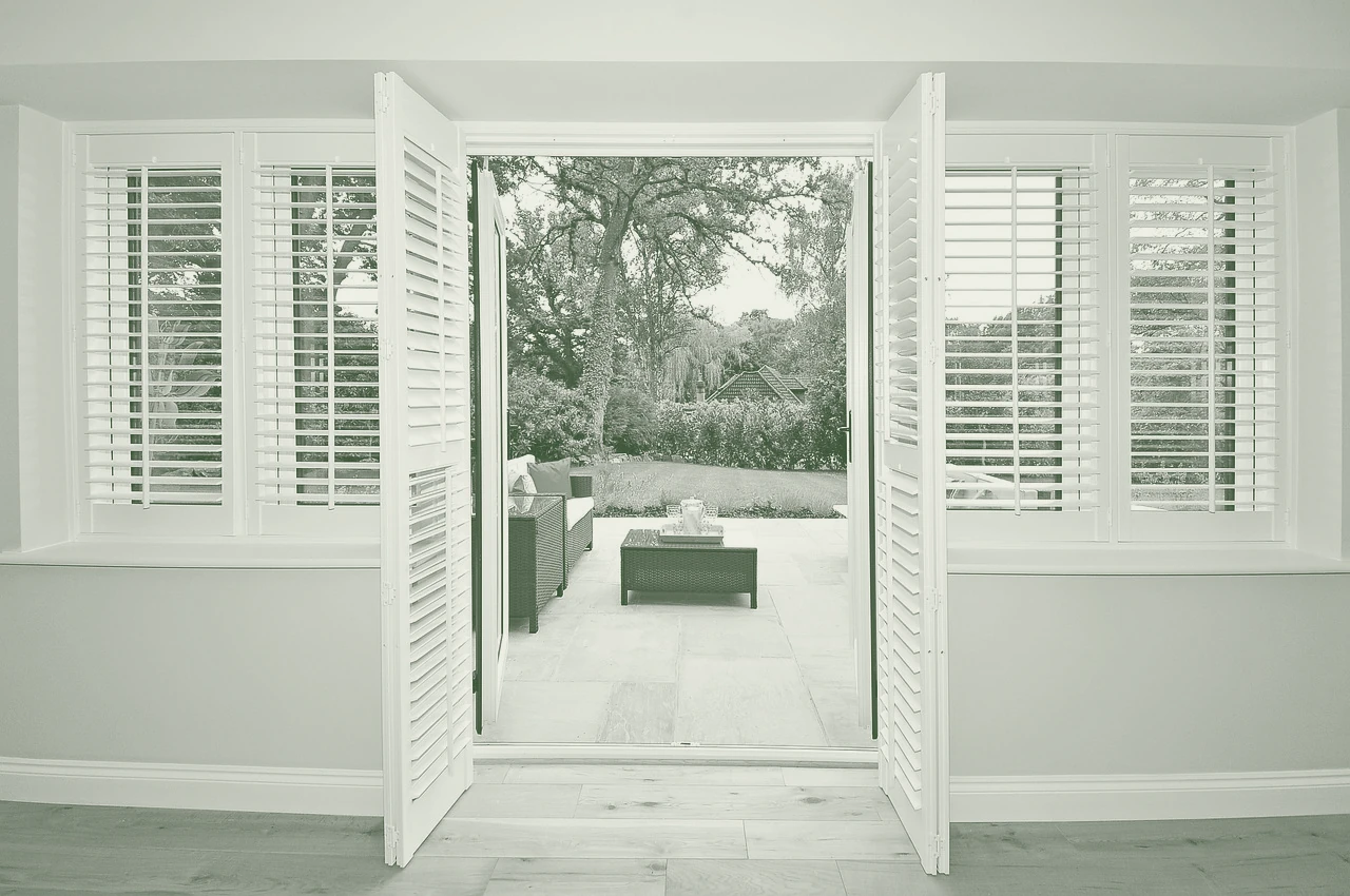 A paved courtyard garden seen through open shutters from a room